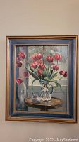 Full view of framed painting showing bouquet of red tulips in crystal pitcher on wooden table.