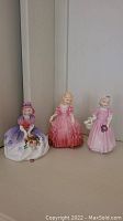 Full view of all three Royal Doulton figurines: Monica, Rose, and Tinker Bell, placed on a white surface.
