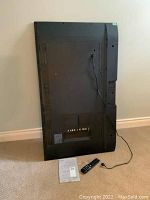 Back view of TV leaning against wall with remote and manual on floor.