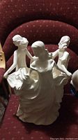 Frontal view of three white porcelain dancing women figurines, one missing part of her nose.