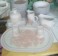 Photo showing the full arrangement of various plates, creamer, sugar bowl, salt and pepper shakers, and serving platter with the pink and cream Love Bird floral pattern on stoneware.