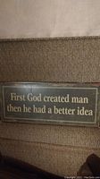 Front view of rectangular metal plaque with the inscription 'First God created man then he had a better idea' in light text on dark metal background.
