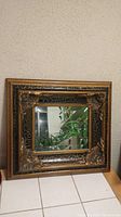 Front view of square beveled mirror with detailed carved frame and gold-black finish.