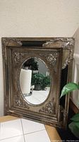 Beveled mirror with oval center mirror and decorative antique silver metal frame, showing minor corner wear on the upper right.