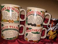 Photo of four vintage ceramic soup mugs stacked and aligned, showing recipe prints and colorful vegetable illustrations including Corn Chowder, Potato Leek Soup, Split Pea Soup, and Vegetable Soup.