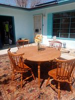 Ethan Allen round dining table with four matching wood spindle back chairs arranged outdoors on rug, with flower centerpiece on table.