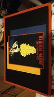 Mounted poster print featuring Champagne Joseph Perrier with cluster of yellow grapes on dark background, orange border.