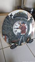 Front view of the limited edition Norman Rockwell collector's plate showing the detailed illustration of a man on ladder adjusting a large clock face with Roman numerals.