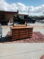 Image showing vintage wooden dresser with 12 drawers and rectangular mirror resting on top, placed on a decorative rug outdoors.