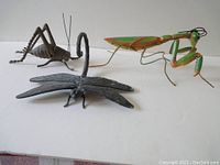 Three vintage metal insect garden sculptures - praying mantis, dragonfly, locust on a white background