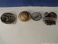 Four belt buckles displayed on a white surface against a blue background, showing all buckles and their designs.