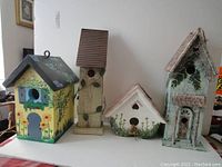 Full group photo showing four different decorative birdhouses of various shapes, colors, and sizes