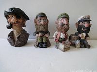 Photo showing all four ceramic figurines lined up, each with unique expressions and clothing details.