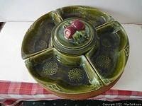 Green ceramic serving platter with 6 sectional pieces arranged around a central lazy susan base with a lid featuring a decorative fruit knob.