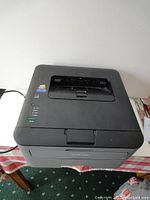 Top view of a Brother HL-L2320D monochrome laser printer on a table showing power indicator lights and paper output tray.