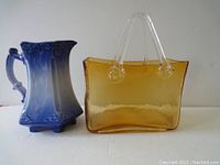 Set showing both the dark blue creamer and orange glass purse shaped vase, side view