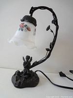 Desk lamp showing curved metal arm with leaves and white floral glass lampshade