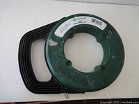 Front view of Greenlee steel fish tape with green reel housing and black handle.