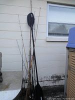 Photo shows 10 fishing rods and 1 black Lifetime canoe paddle leaned against a wall.