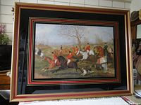 Framed print showing full view of fox hunting scene with riders in red coats on horses and hunting dogs in countryside setting.