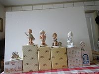 Front view of five Enesco figurines displayed on their original Enesco boxes and one Lilliput Lane boxed figurine in original packaging seen on the left side.