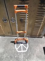 Front view of collapsed hand cart showing frame, handle, and base platform on pavement.