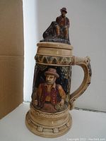 Full view of the large beer stein showing the painted figurative design, handle, and lid setup.
