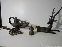 Four brass figurines displayed together: an Aladdin lamp, brass deer, bell, and canon model