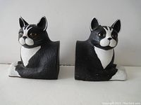 Front view of the pair of black and white ceramic cat bookends, showing both cats sitting with differing eye colors.