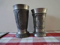 Pair of German pewter cups with embossed cityscape designs showing size difference and general shape.