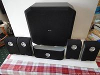 Full surround speaker set including subwoofer, center channel, and four satellite speakers laid out on a table
