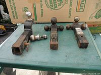 Three metal towing receivers with attached trailer balls and one spare trailer ball displayed on a surface. Rust and wear are visible on all items.