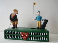Front view showing the green base with grooves and two golfer figurines, a player and a caddy holding a flag and bag.