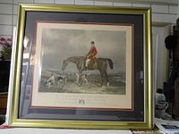 Front view of the framed colored print depicting a fox hunter on horseback with hounds.
