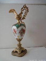 Full view of vintage ewer with porcelain body and ornate metal handle and base on stone platform
