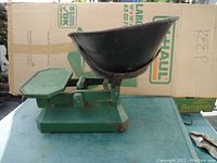 Side view of vintage green metal balance scale with black weighing bowl and flat platform.