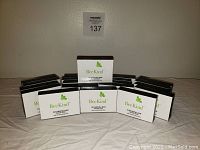 Twenty bars of BeeKind Cleansing Soap stacked on a white sheet, showing front packaging with product name and logo.