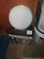 Round LED ceiling light fixture sitting on top of the Artika Skyraker product box in a storage area