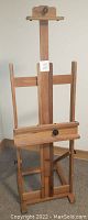 Full front view of the wooden easel showing its frame, adjustable canvas holders, and base.