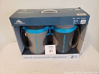 Front view of boxed set of two High Sierra insulated water bottles/jugs, grey with blue lids, brand visible on bottle and packaging.