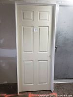 Full view of a white 6-panel interior door installed within its frame, leaning against a wall, in new condition.