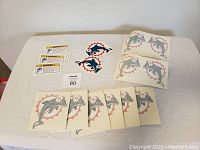 Multiple sheets of Miami Dolphins stickers and decals laid out on a white surface, showing dolphin logos and helmet safety warning stickers.