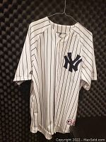 Full view of men's white New York Yankees pinstripe baseball jersey hanging on wire hanger, showing front button closure and large navy interlocking NY logo on chest.