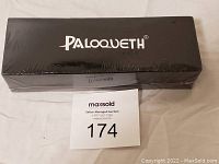 Photo shows a black rectangular box with the brand name Paloqueth printed on top. The box appears sealed with shrink wrap. Minor damage to packaging is visible. Maxsold lot number 174 card placed in front.