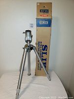 Full view of vintage tripod extended in front of original Slik Master box standing upright showing brand and origin details.