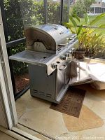 Side view of Char-Broil gas grill with side burner, control knobs, and hinged lid on patio.