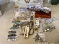 Wide view of assorted costume jewelry pieces including multiple plastic bags with beads, loose pieces, and some chains, with a jewelry box visible.