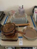 Glass bakeware and measuring cups on table, visible amber glass pots, clear rectangular and round baking dishes, and measuring cups.