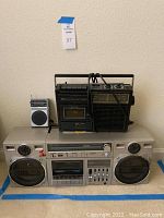Overview of all three audio devices—the Magnavox stereo on bottom with dual cassette decks; the Sears AM/FM radio cassette recorder with carrying handle and analog tuning on top right; and the compact Soundesign pocket radio on top left.