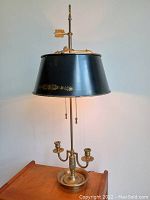 Full view of the lamp showing the black tole adjustable shade with floral detailing, brass base with two candle holders, and the pull chains.